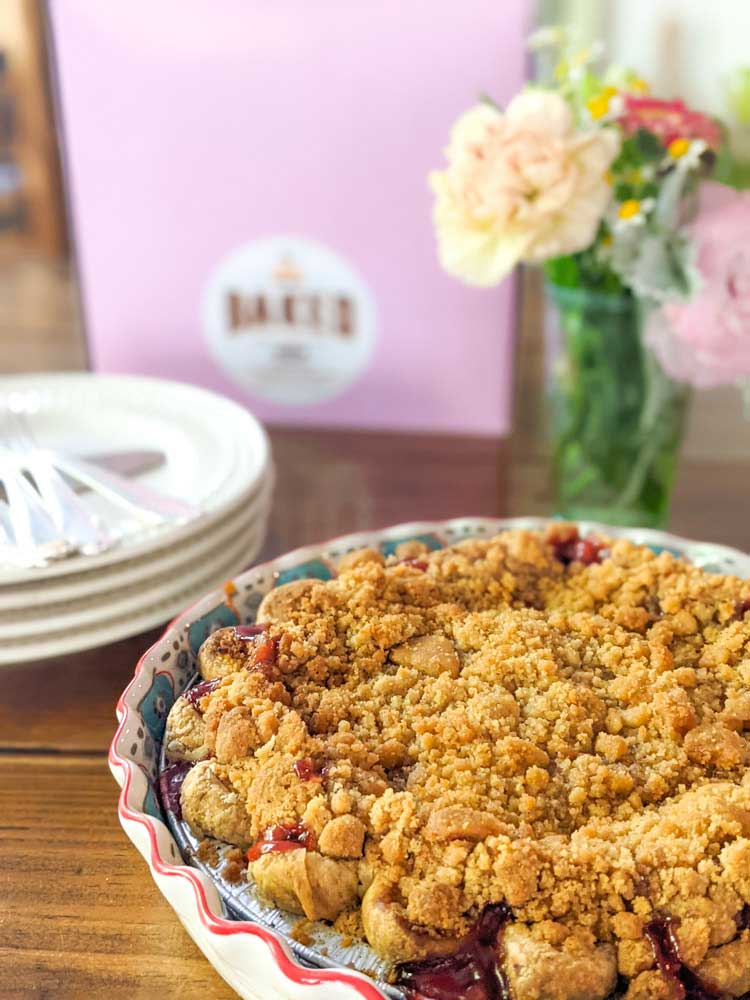 Cherry Crumb pie in the front with flowers, plates and a pie box in the background