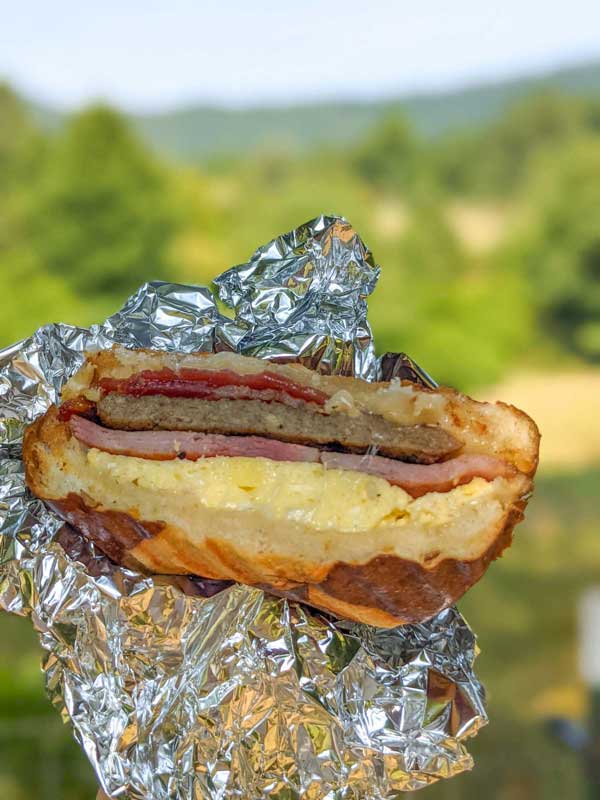 Lumberjack sandwich with layers of bacon, ham, sausage and egg on a pretzel roll