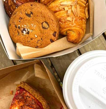 A box of pastries from OWL Bakery along with a coffee in a to go cup and a pink beet chèvre quiche