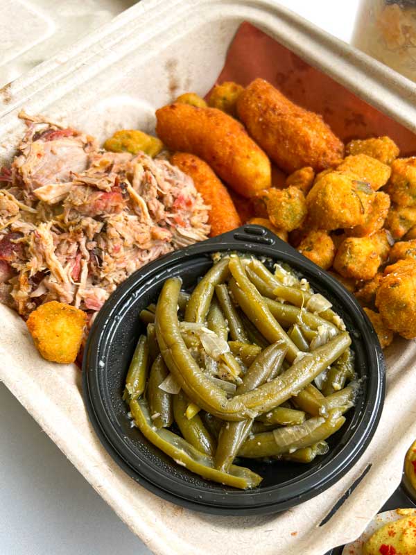 takeout box with barbeque, green beans, fried okra, and hush puppies from Luella's Barbeque