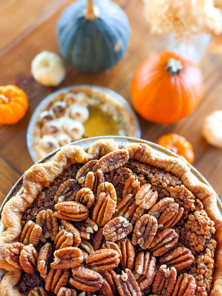 Pecan pie topped with tons of pecans with another pie and pumpkins in the background