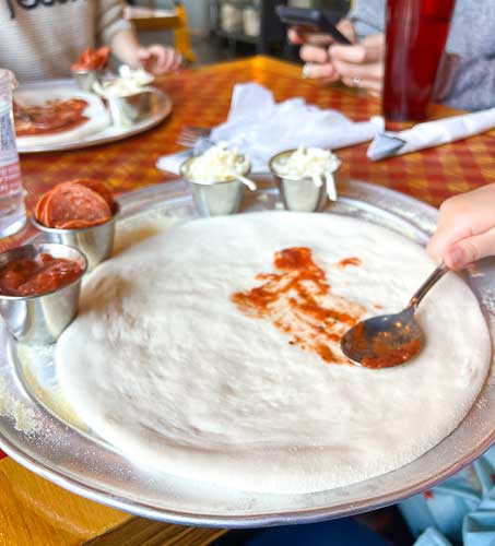 Pizza dough, a cup of tomato sauce, pepperoni and cheese at Pizza Mind for kids to build their own pizza